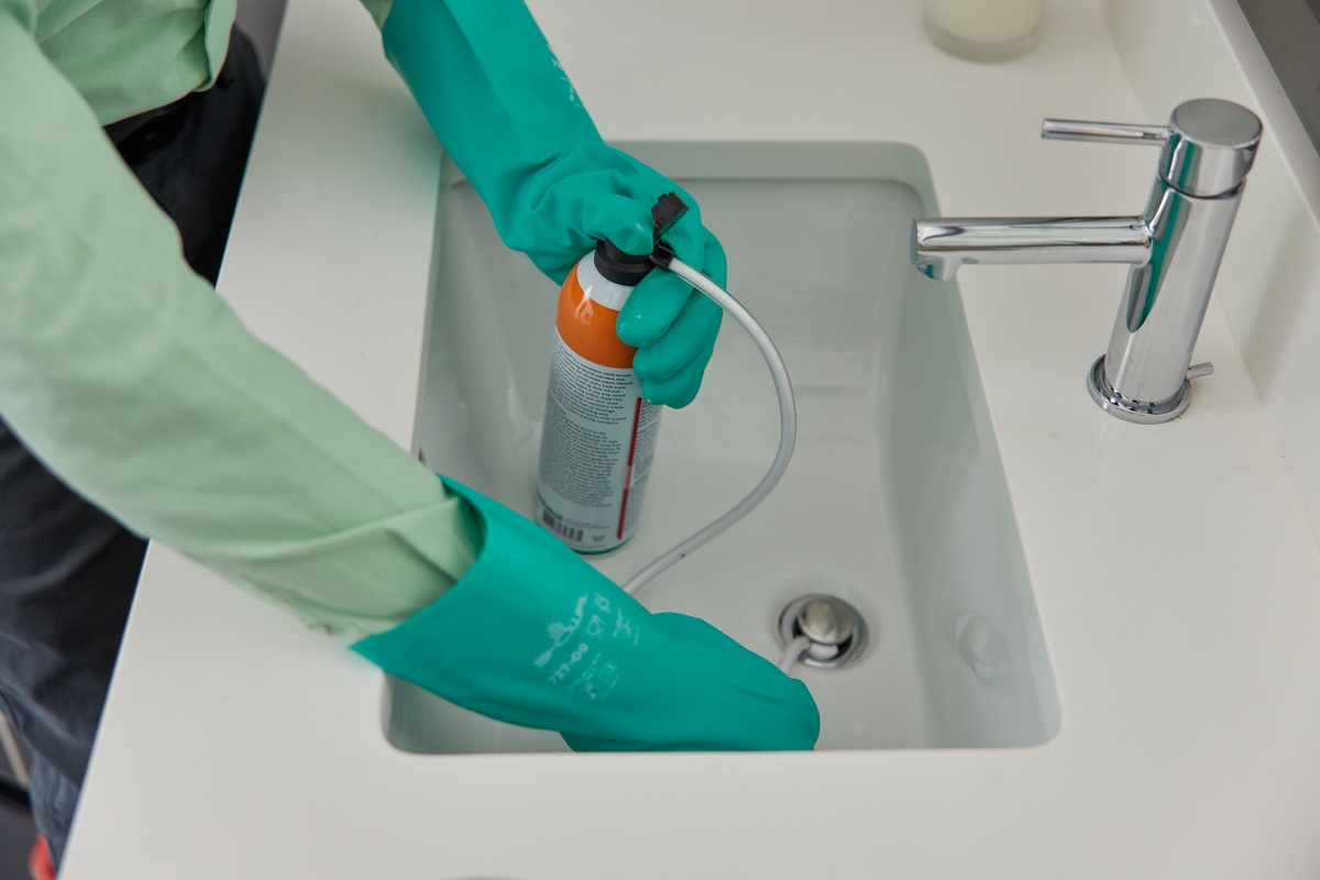 Pest Control Service Treating Sink Drain Service pro using treatment in sink drain